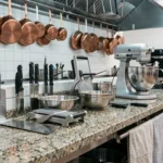 Équipement de cuisine professionnelle disposé sur un plan de travail en granit avec couteaux, robot pâtissier et ustensiles en acier inoxydable